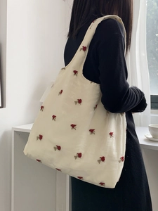 Gros plan sur la broderie rose rouge d'un sac cabas en toile beige avec bandoulière