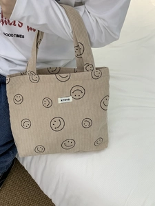 Detail of beige corduroy tote bag featuring black smile prints and white brand label