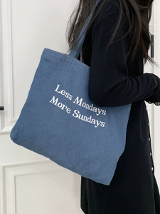 Close-up of denim tote bag featuring white Less Mondays More Sundays embroidery detail