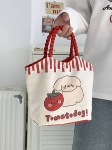 Close-up of cream canvas tote with red woven handles and tomato dog print detail
