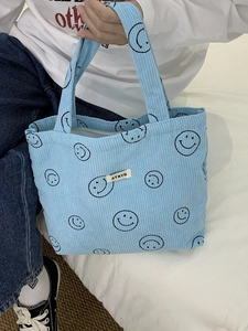 Close-up of light blue corduroy tote bag with black smiley patterns and textile label