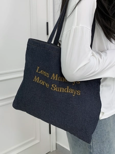 Detail of blue denim tote bag with yellow 'Less Mondays More Sundays' embroidery