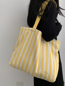 Rear view of model wearing a large capacity yellow and white striped canvas tote bag