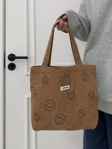 Close-up of brown corduroy tote bag featuring black smiley faces and woven logo tag