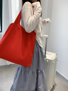 Detailed side view of a large red canvas tote bag with wide shoulder straps worn by model
