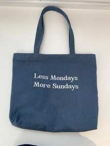 Detail of blue denim tote bag with white 'Less Mondays More Sundays' embroidery