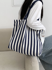 Blue and white striped canvas tote bag shown as a spacious shoulder bag on a model