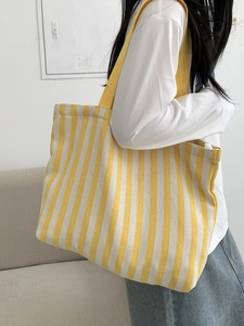Detail of high-capacity striped canvas tote bag with wide shoulder strap on model