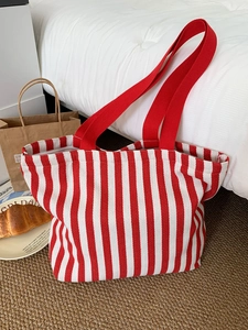 Detail of red and white striped canvas tote bag with wide red straps on a cozy bed