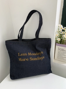 Detail of dark blue denim tote bag featuring yellow embroidery text on white stand