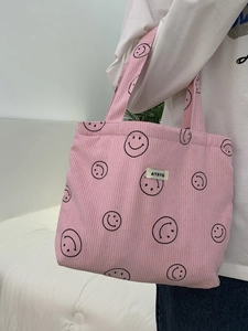 Close-up of pink corduroy tote bag featuring black smiley patterns and a woven logo label
