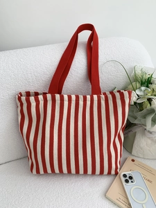 Detail of red and white striped canvas tote bag with shoulder straps on a sofa