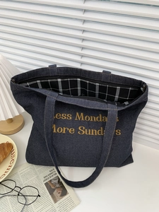 Detail of blue denim tote bag with yellow embroidery and checkered lining on a white desk