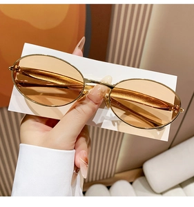 Macro detail of oval sunglasses with gold metal frame and translucent orange lenses