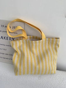 Detail of yellow and white striped canvas tote bag with durable woven handles on a prop board