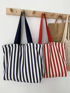 Large striped canvas tote bags in red and blue displayed on minimalist wooden hooks