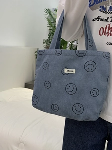 Detail view of the blue corduroy tote bag featuring a black smiley face and brand label