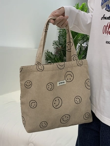 Detail of beige corduroy tote bag featuring a black smiley face print and logo label