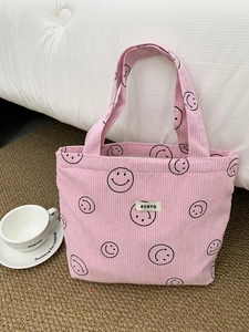 Pink corduroy tote bag with black smiley patterns and a woven label on a textured rug