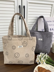 Detail of corduroy tote bags with smile patterns and brand label on a wooden desk
