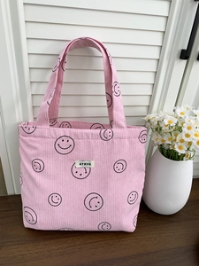 Detailed view of pink corduroy tote bag with smile patterns and logo on wooden table