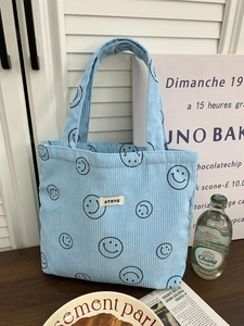 Detail of light blue corduroy tote bag featuring smiling face patterns and ATRYG label