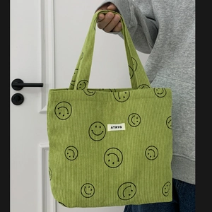 Close-up of light green corduroy tote bag featuring black smiley face patterns and brand tag