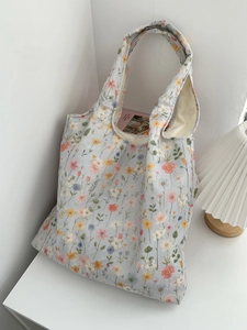 Détail d'un sac cabas en toile bleu clair avec broderies florales colorées et style épuré