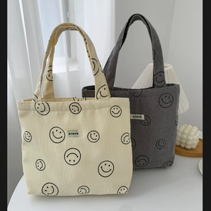 Detail of corduroy tote bags with smiley patterns in off-white and dark gray colors