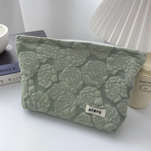 Close-up of sage green makeup bag featuring embossed rose floral texture and cloth brand tag