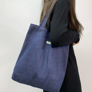 Detail view of washed dark blue denim tote bag featuring minimalist brand woven label