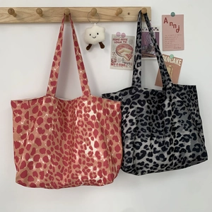 Large leopard print canvas tote bags in red and grey hanging on a wooden rack