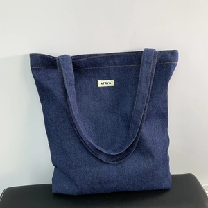 Detailed shot of the ATRYG logo tag and yellow stitching on dark denim tote bag