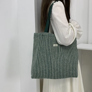 Detail showing the green herringbone knit fabric texture and ATRYG logo on a tote bag