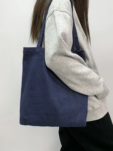 Detail view of large dark blue denim tote bag with wide shoulder strap on model