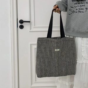 Detail view of large herringbone wool tote bag with black woven handles and logo