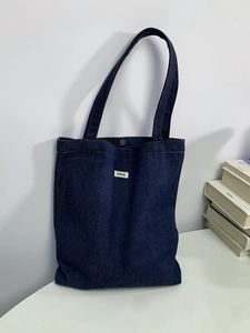 Detail view of deep blue denim tote bag featuring white ATRYG patch and metal snap closure