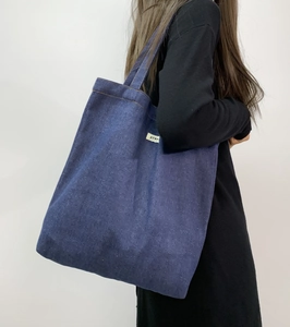 Detail of blue denim tote bag with ATRYS brand label and yellow stitching trim