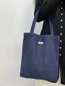 Detail of dark blue denim tote bag showing the textured fabric and white woven label