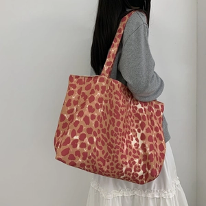 Close-up of leopard print canvas tote bag carried by a model against a white wall