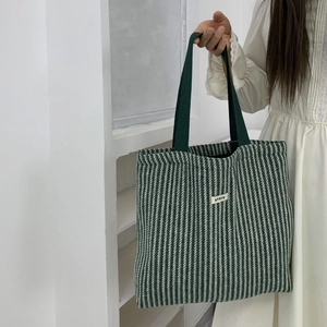 Detail of green herringbone striped tote bag featuring ATRYG woven label and handles