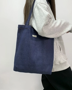 Detail view of large dark blue denim tote bag with white logo label worn by model