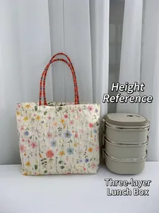 Floral canvas lunch bag with orange rope handles next to a 3-tier food container