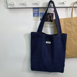 Detail of dark blue denim tote bag with white logo label hanging on a wooden rack