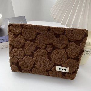 Detail of a brown cosmetics bag with 3D embossed rose pattern and brand label