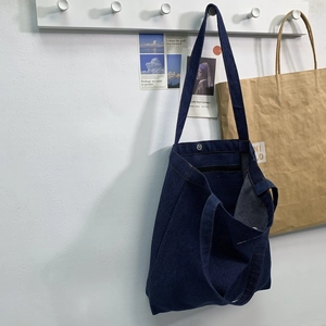 Close-up of dark blue denim tote bag featuring silver snap button and interior zipper pocket