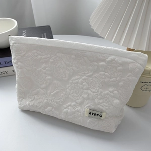 Close-up of white rose embossed fabric cosmetic bag with zipper and logo detail