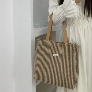 Detail of a brown striped canvas tote bag with woven handles and white brand label