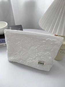 Detail of white embossed rose texture on fabric cosmetic bag with zipper and brand label