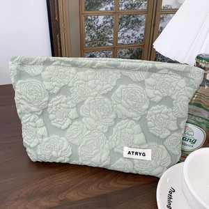 Detail of light green cosmetic bag with rose floral embossing and fabric label
